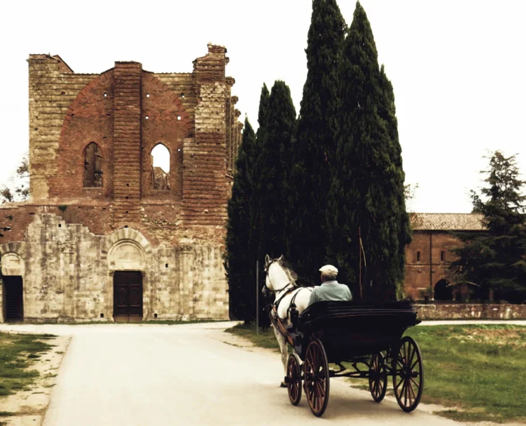 L'abbazia di San Galgano senza tetto tra i cipressi, con una carrozza davanti