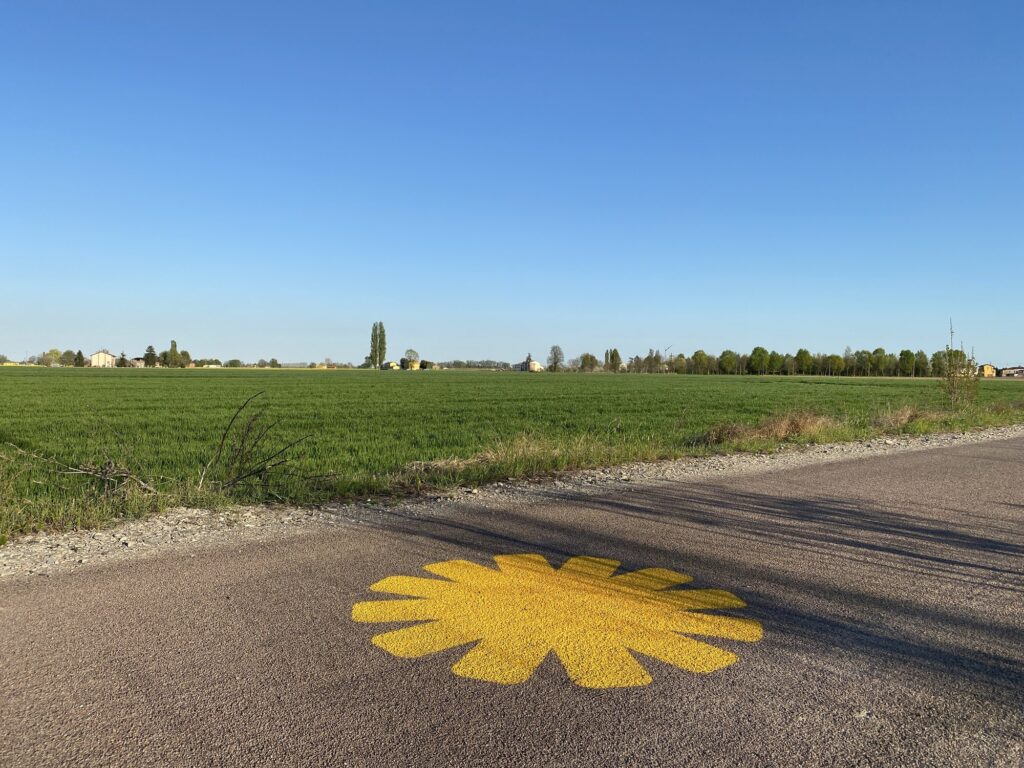 Il sole giallo dipinto sulla Ciclovia del Sole tra i campi della Bassa emiliana