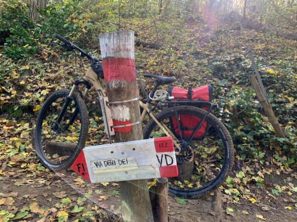 Bicicletta con le borse appoggiata a un palo con il segnavia bianco e rosso della Via degli Dei, tra le foglie d'autunno