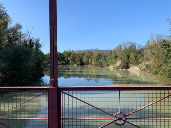 Il Reno e le colline boscose dietro la ringhiera rossa del ponte di Vizzano