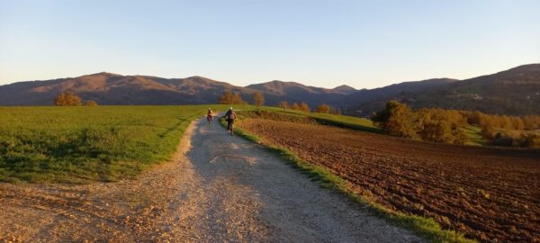 Sterrato tra i campi arati, con due ciclisti e i monti del Mugello
